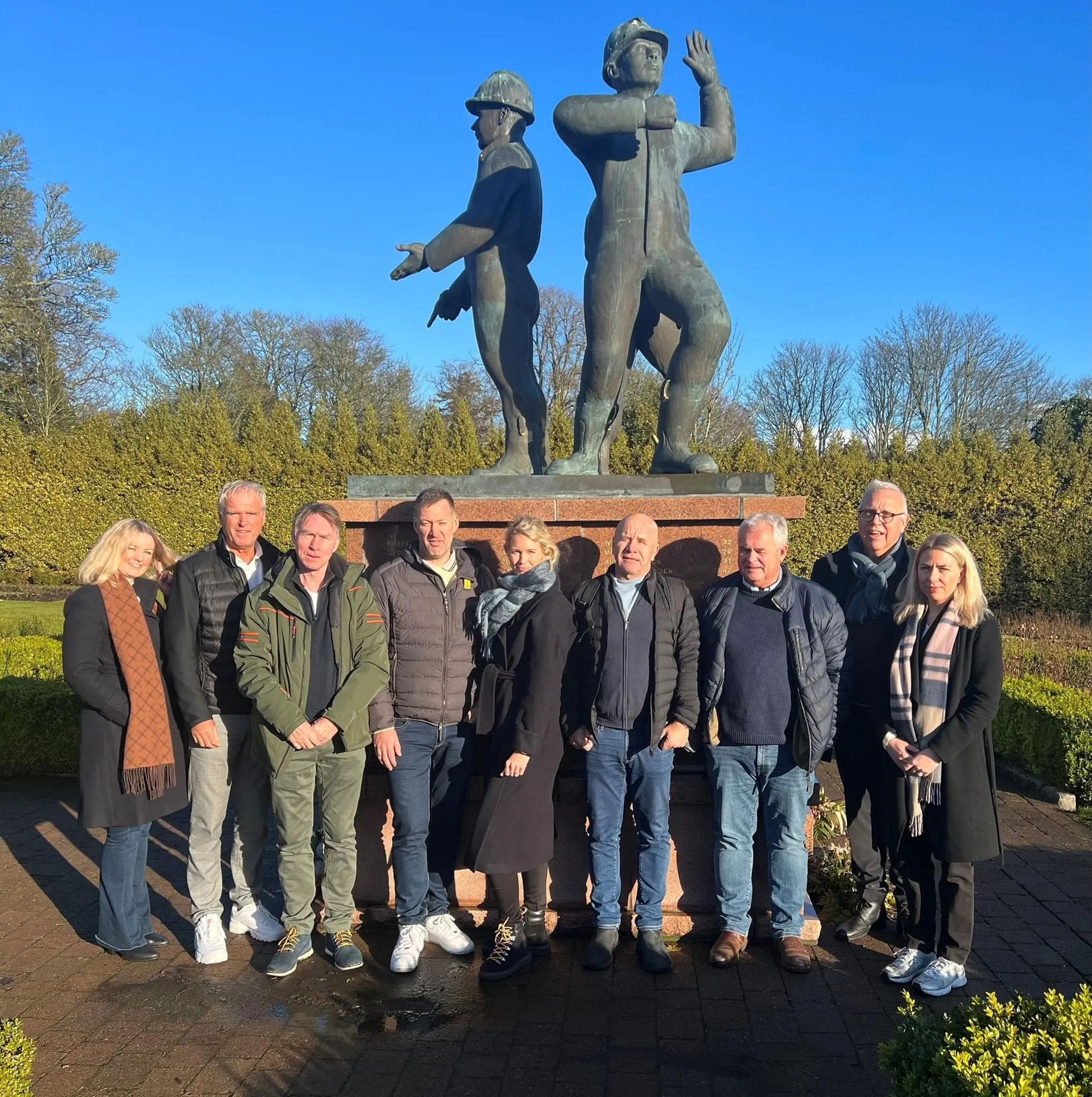 En gruppe medlemmer og tillitsvalgte i Lederne står foran en bronsestatue av to oljearbeidere.